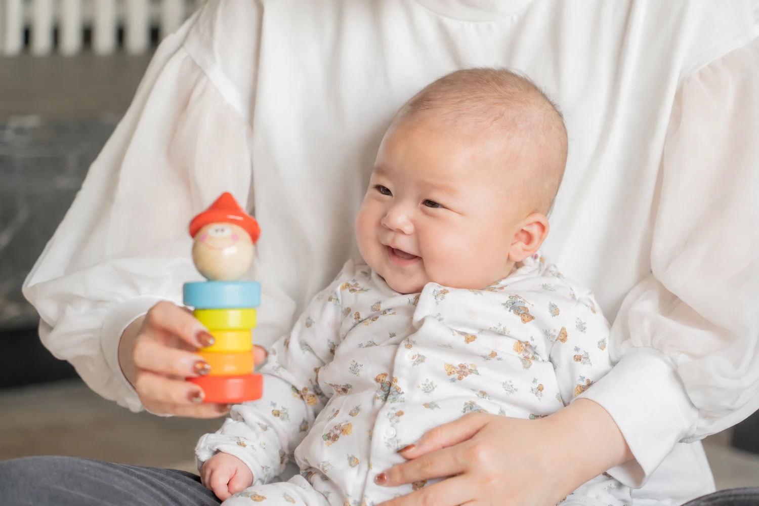 保護者のひざで、カラフルな木のおもちゃを見ながらほほえむお子さま