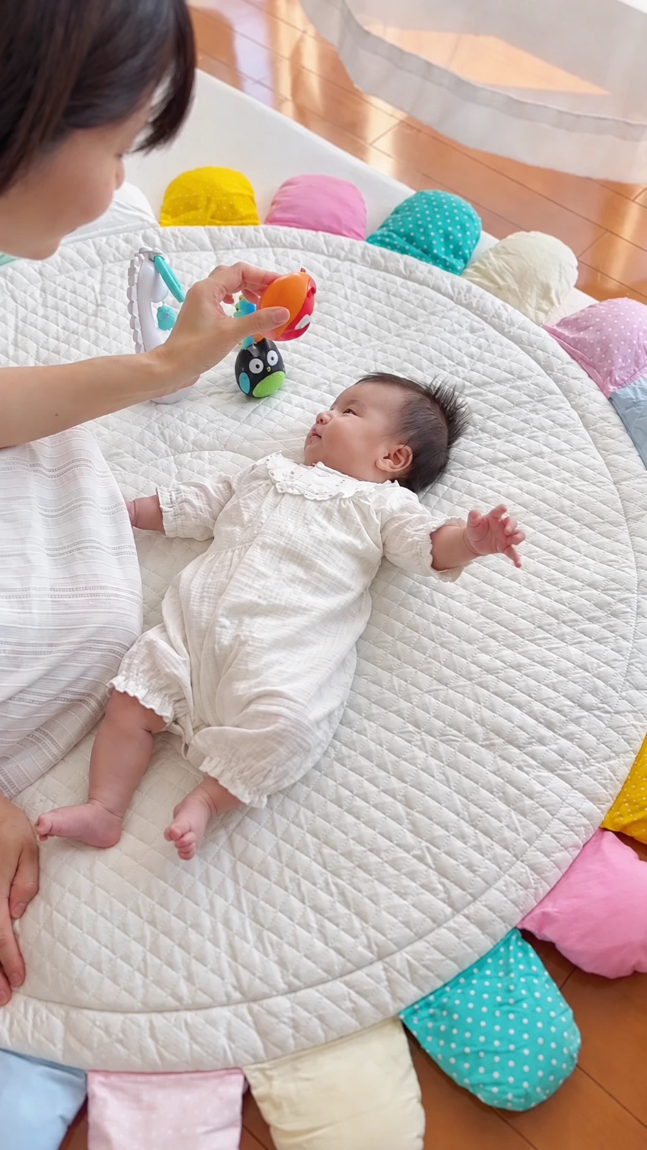 届いたおもちゃを保護者が見せ、花びらのマットの上でお子さまが見つめる場面。お届け事例動画のカバー