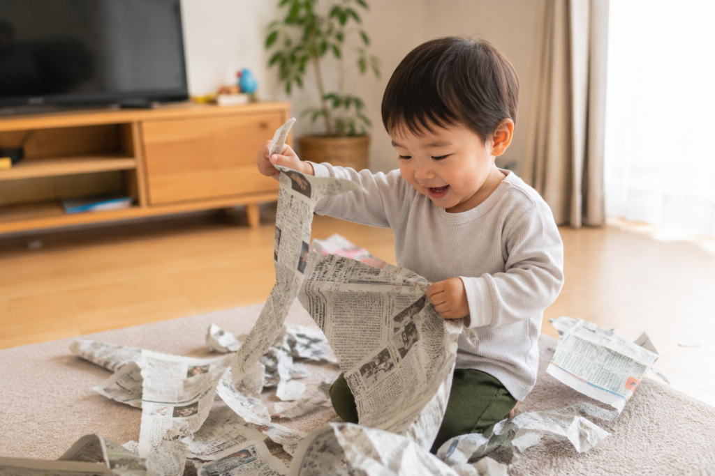 リビングで新聞紙を使って遊ぶ2歳児の様子