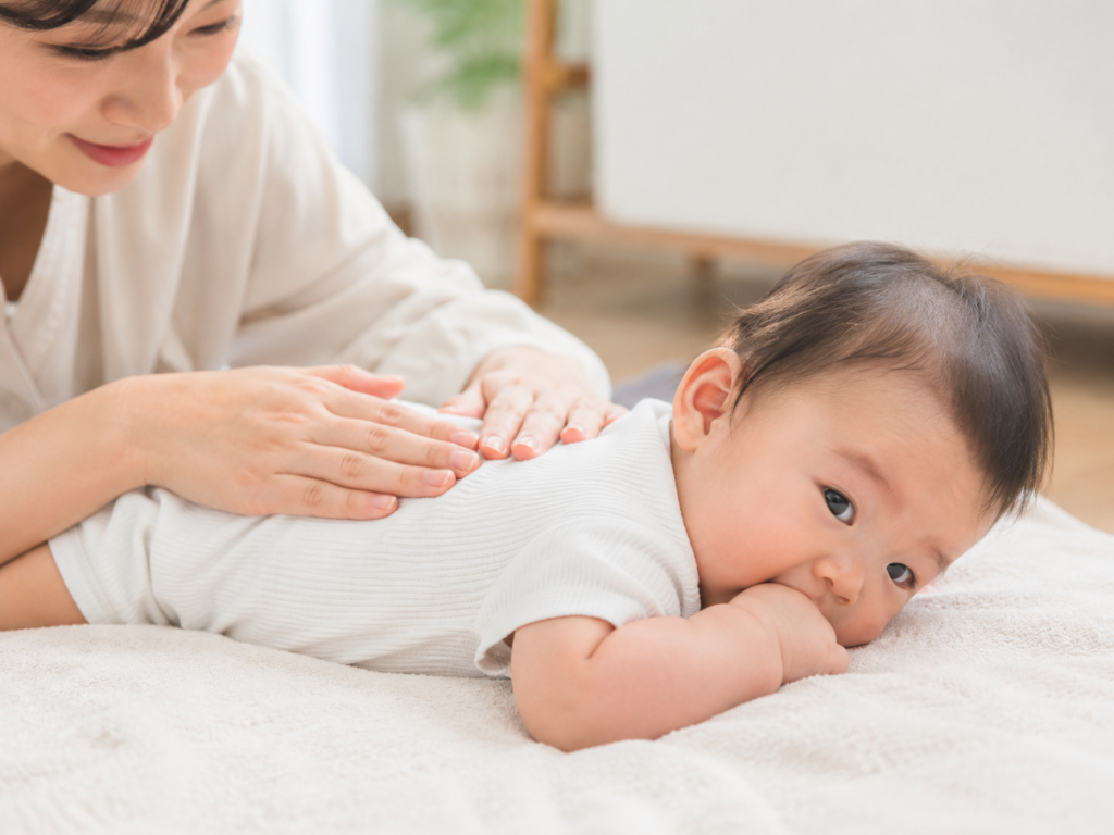 赤ちゃんをうつ伏せにしてやさしく背中をさする親の手元の写真